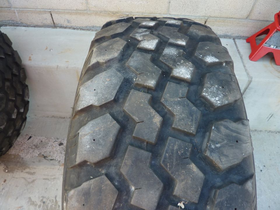 Off-road tire with aggressive tread pattern, next to another tire. Red jack visible in background
