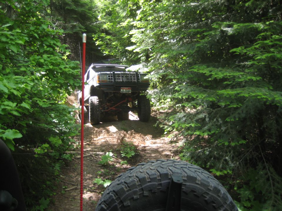 Modified off-road Jeep Cherokee XJ climbing a dirt trail, front grille and bumper visible