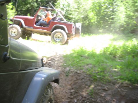 2005 Jeep Wrangler - Two Jeeps navigate a muddy, wooded trail on a sunny day.