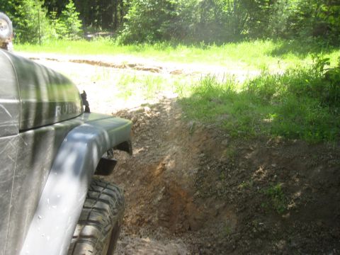 2005 Jeep Wrangler - A Jeep Wrangler navigates a muddy trail surrounded by lush green foliage.