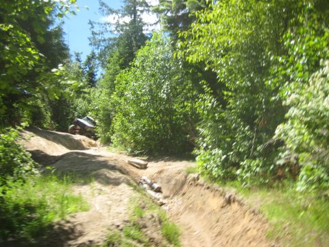 2005 Jeep Wrangler - An off-road vehicle navigates a challenging dirt trail through a dense forest on a sunny day.