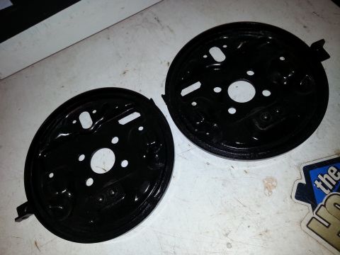 1991 Ford Festiva - Two black brake dust shields are shown, likely for a vehicle's rear drum brakes.