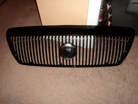 2004 Mercury Grand Marquis - A close-up of a black Mercury grille with vertical slats and a circular emblem.