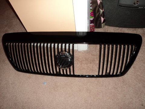 2004 Mercury Grand Marquis - A black grille with vertical slats and a central Mercury emblem is displayed against a carpeted surface.