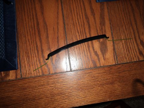 2004 Mercury Grand Marquis - A black plastic trim piece, likely for a car grille, lies on a wooden surface with attached yellow clips.