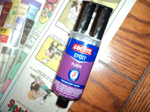 2004 Mercury Grand Marquis - A tube of Loctite Epoxy Plastic is shown with its dual applicators extended, resting on a newspaper and a wooden surface.