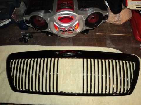 2004 Mercury Grand Marquis - Glossy black vertical-bar aftermarket grille resting on a bench, with a silver boombox stereo in the background.