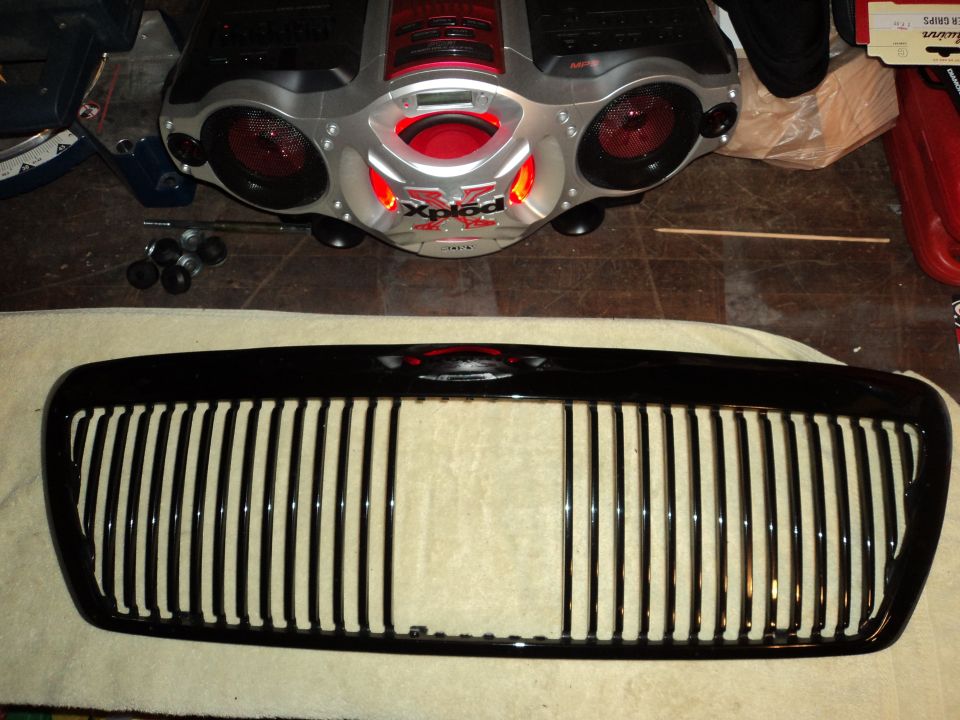 Glossy black vertical-bar grille on a workbench with a boombox behind