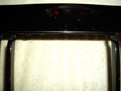 2004 Mercury Grand Marquis - Close-up of a black car grille with chrome accents, showing a reflection of a red light.