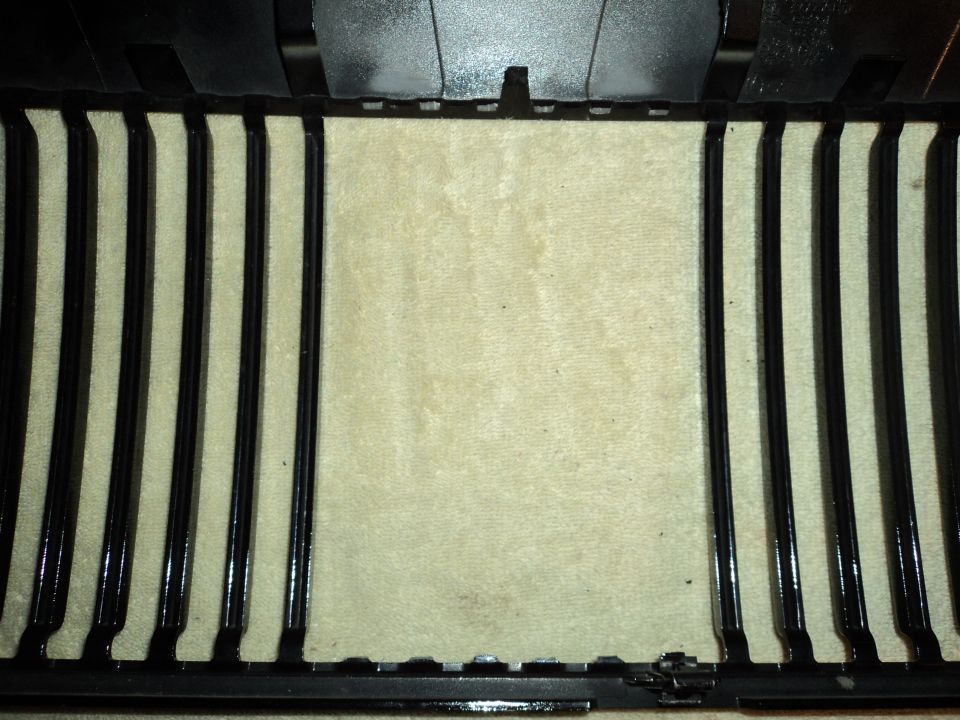 Close-up of a car's black vertical grille slats with a beige textured background