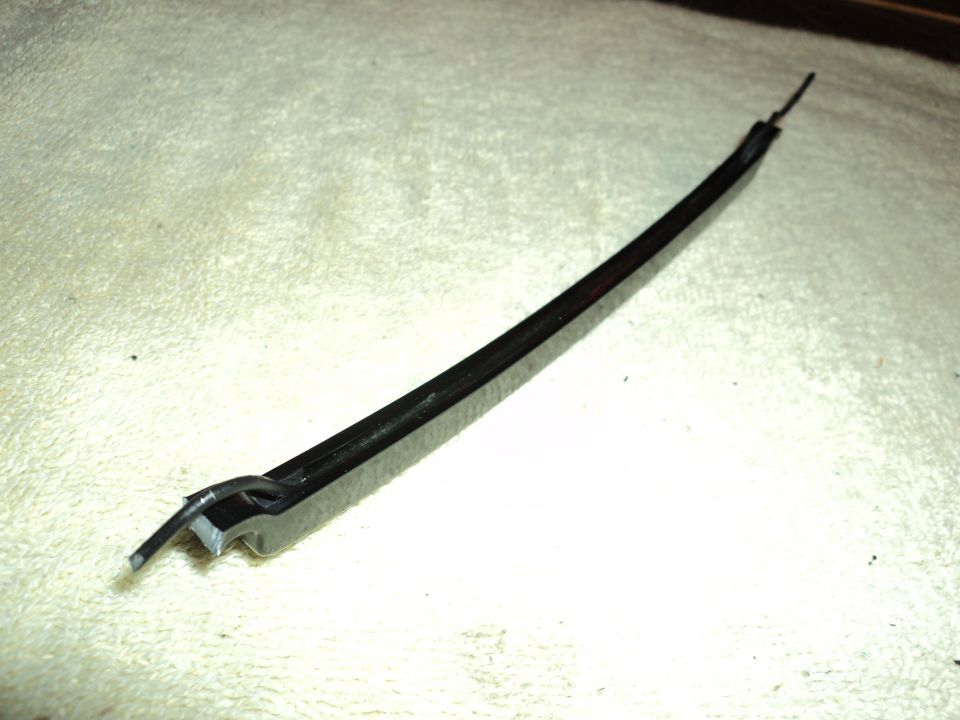 Black automotive trim piece with metal clip, lying on textured surface