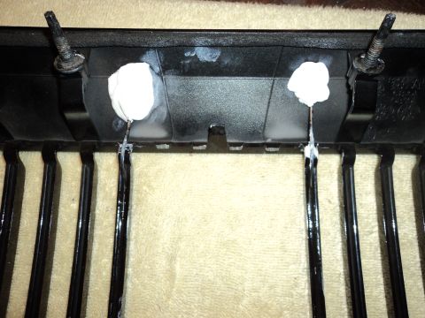 2004 Mercury Grand Marquis - Close-up of a black car grille showing repair work with white adhesive on the mounting points.