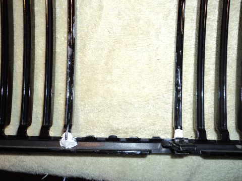 2004 Mercury Grand Marquis - Close-up of a black grille with chrome vertical bars, adhesive repairs on the mounting points.