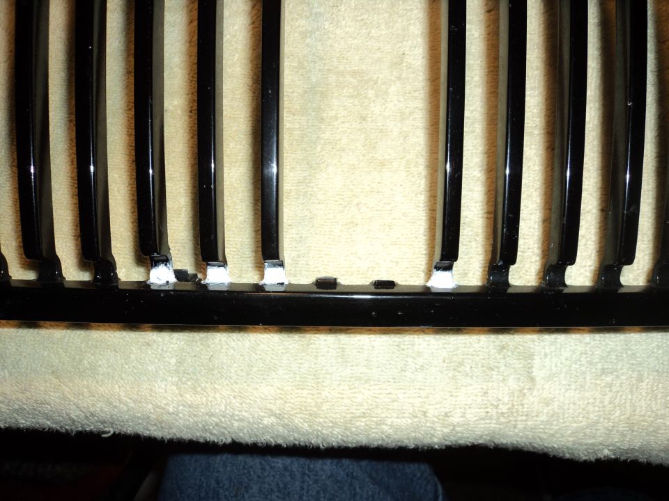 Close-up of a black car grille with white adhesive on the bottom of some vertical bars