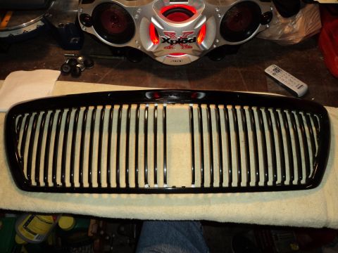 2004 Mercury Grand Marquis - A black vertical slat grille is laid out on a surface, with a car audio system visible in the background.