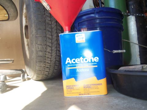 1968 Ford Bronco - A can of Acetone is being poured into with a red funnel, with a tire and buckets in the background.