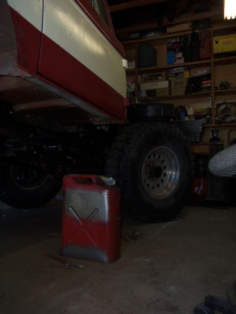 1968 Ford Bronco - A red jerry can sits on the floor of a garage next to the undercarriage of a vehicle with large tires.