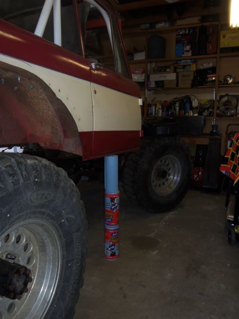 1968 Ford Bronco - A red and white 1968 Ford Bronco is shown in a garage, lifted with large off-road tires.