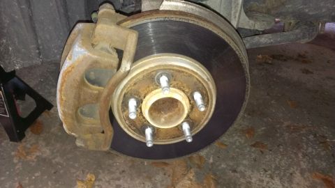 2003 Mercury Marauder - Close-up of a vehicle's brake system, a rusty caliper and a worn rotor, with a jack stand in the background.