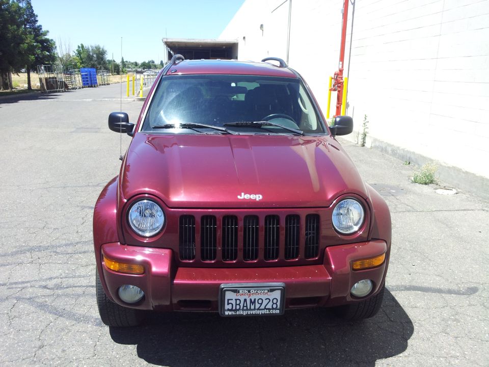 Red Jeep Liberty parked outside a building. Front view shows the grille, headlights, and license plate