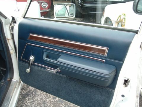 1991 Ford LTD Crown Victoria - The interior door panel features blue vinyl and fabric with wood grain trim and a chrome window crank, seen alongside other vehicles.