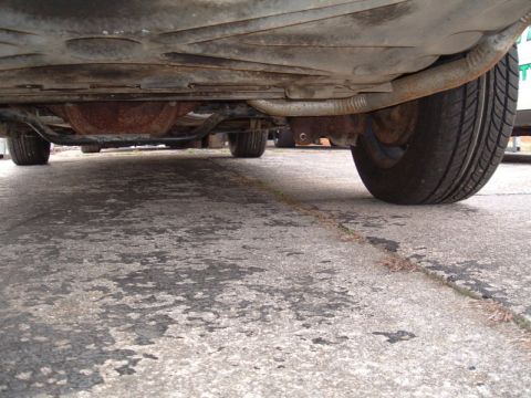 1991 Ford LTD Crown Victoria - A low-angle shot reveals the undercarriage of a vehicle, including its exhaust system and tires on a paved surface.
