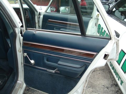 1991 Ford LTD Crown Victoria - The interior of a police car shows blue door panels with wood trim. Text on an adjacent vehicle reads 'COUNTY'.