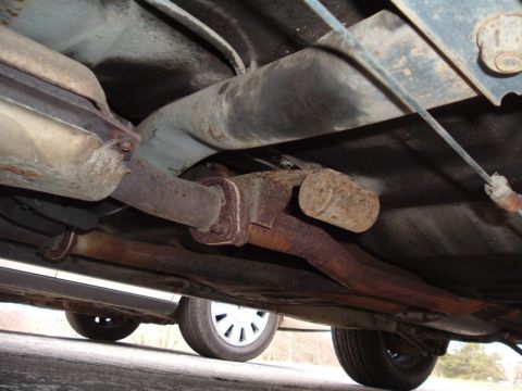 1991 Ford LTD Crown Victoria - Underside view of a car's exhaust system and rear wheel, showing signs of rust.