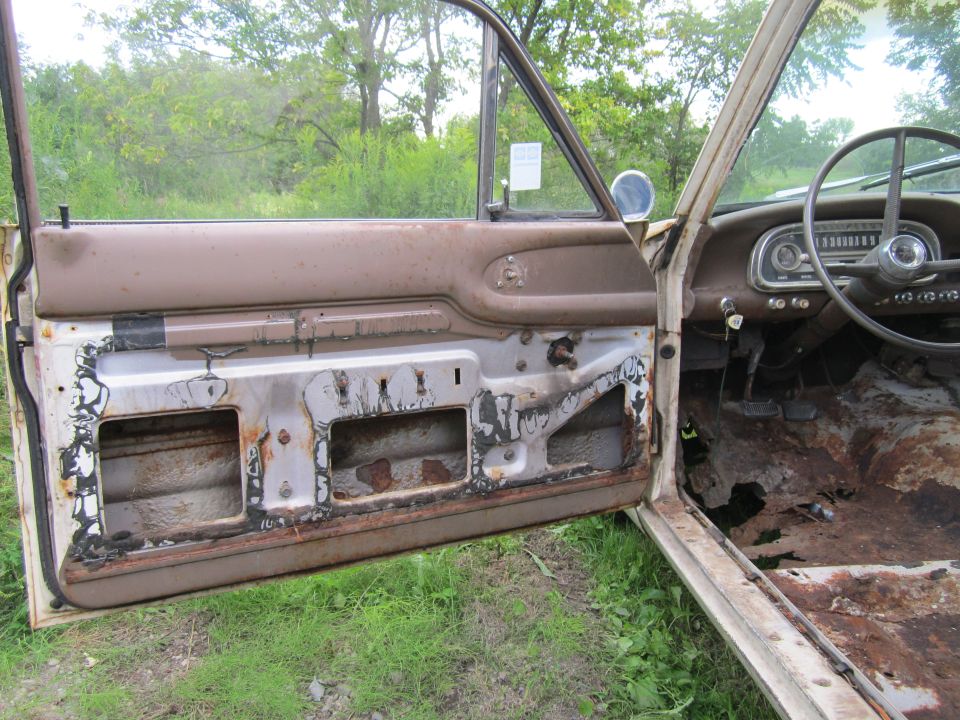 Open driver's door with panel removed showing rust on a white 1963 Ford Ranchero, rusted floor visible inside