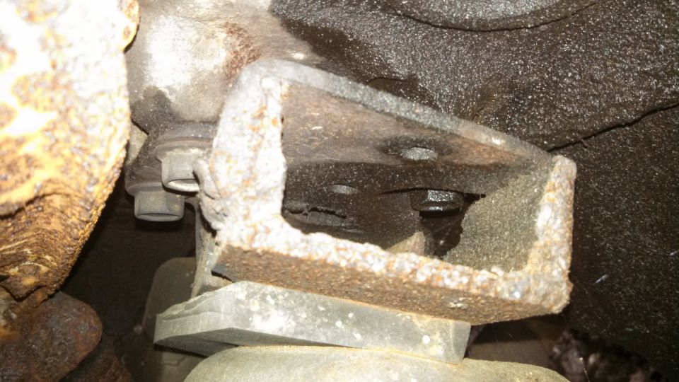 Close-up of a rusted metal bracket with a bolt, likely part of a vehicle's undercarriage