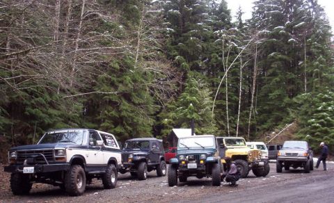 1982 Ford Bronco - A group of off-road vehicles are parked on a dirt road in a wooded area with snow on the trees.