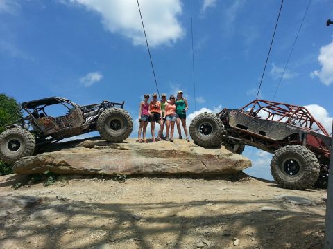 1967 Ford Mustang - Two custom off-road vehicles are positioned on a rocky terrain with four individuals standing between them under a bright sky.