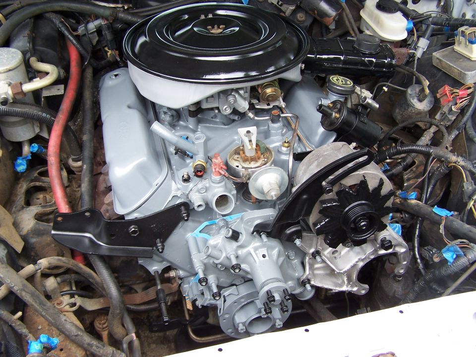 Photo of a V8 engine mounted in an engine bay with carburetor, air cleaner, and accessory brackets.