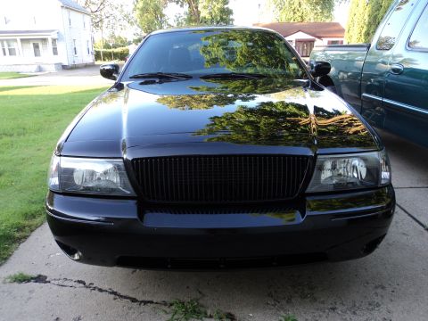 2004 Mercury Grand Marquis - Front end of a black Mercury Grand Marquis with a murdered-out vertical-bar grille and clear headlights, parked in a driveway.