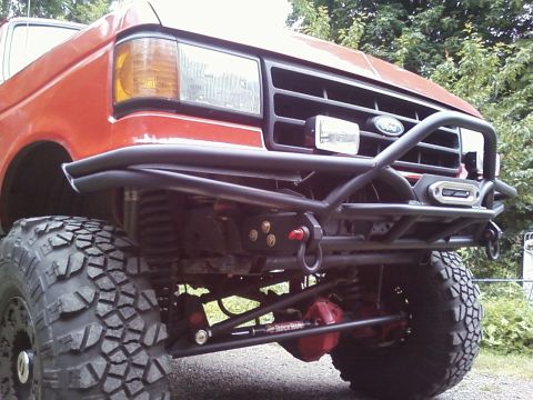 1989 Ford Bronco - Front view of a red truck with a custom bumper and off-road tires, showing the Ford grille.