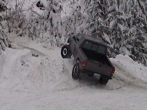1982 Ford Bronco - A gray pickup truck navigates a snow-covered hill with its wheels angled.
