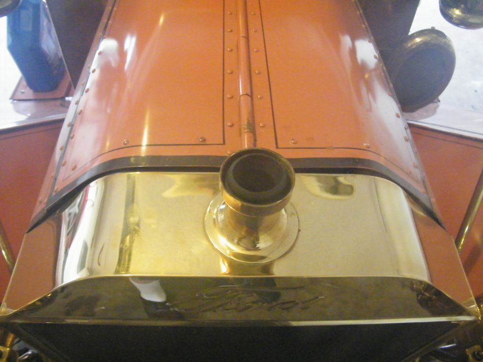 Brass radiator shell with embossed Ford script and filler neck seen over a riveted red hood