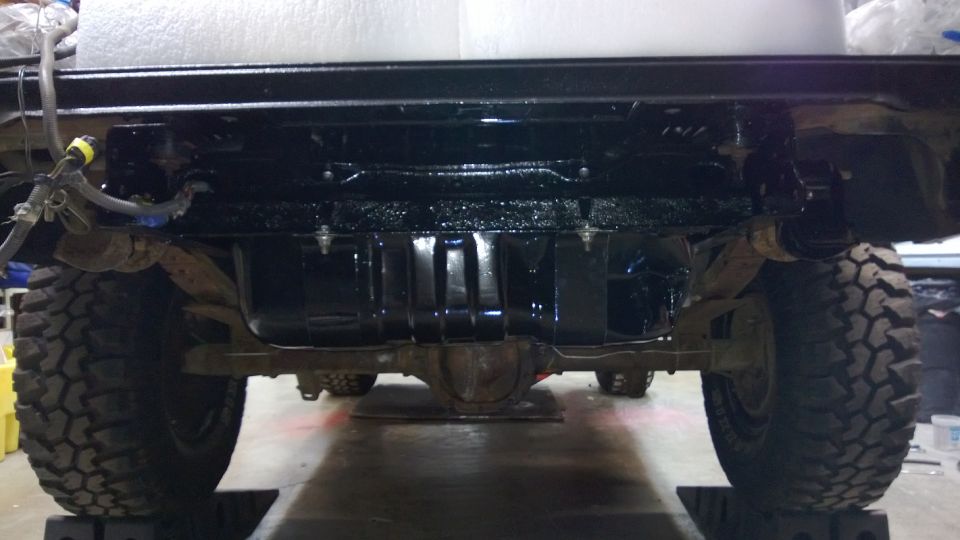 Undercarriage view of a vehicle with large tires and a black fuel tank