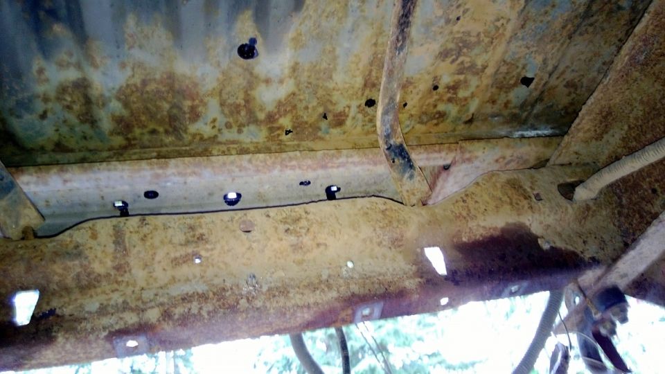 Heavily rusted undercarriage frame rails and crossmembers with visible holes and mounting points