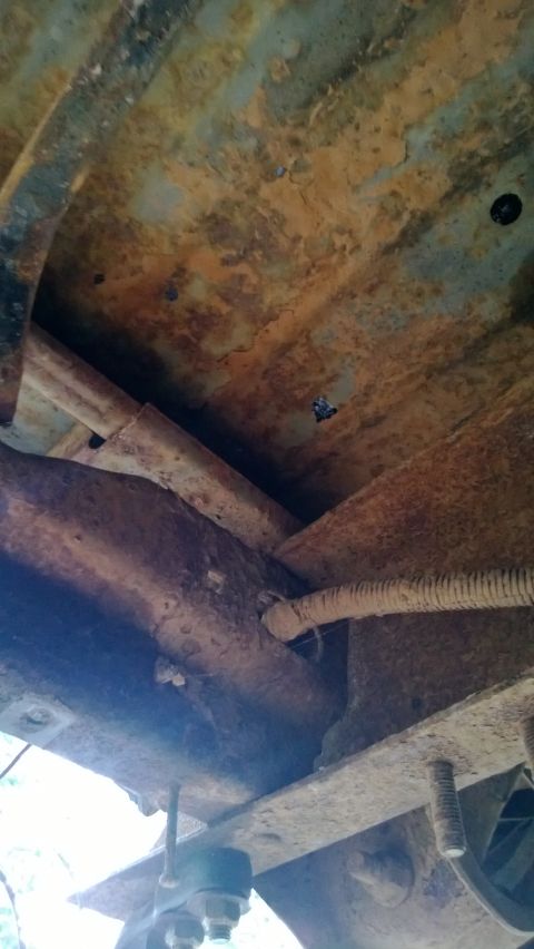 1983 Ford Bronco - The heavily rusted undercarriage of a vehicle is visible, with frame rails and exhaust pipes showing significant corrosion.