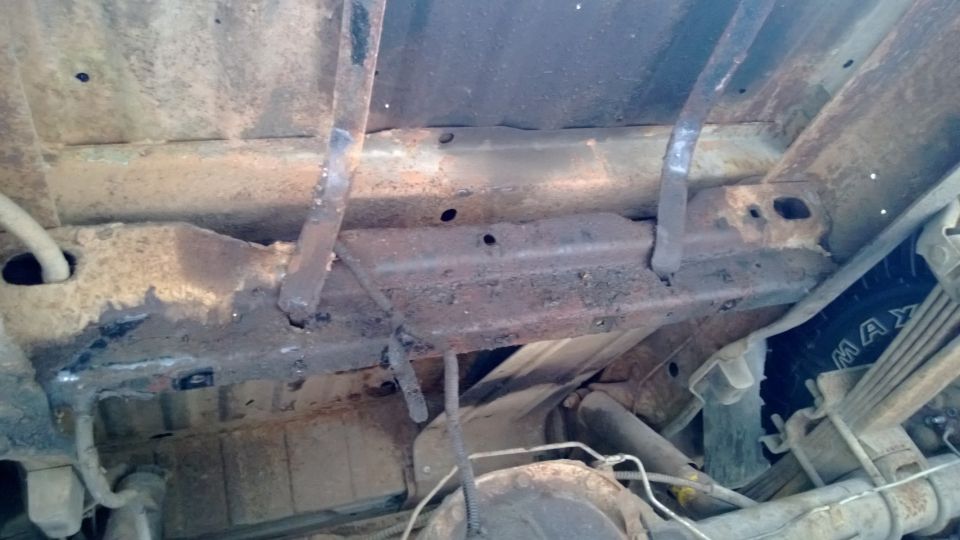 Underside view of rusty frame rails, suspension components, and part of a tire