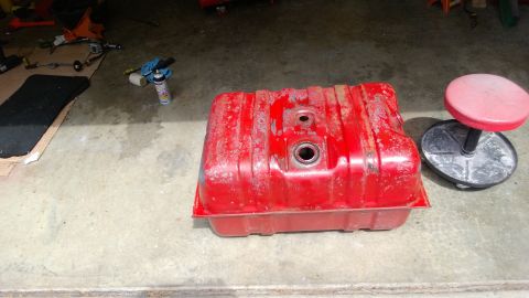 1983 Ford Bronco - A red fuel tank, likely for a vehicle, rests on a garage floor with tools and a stool nearby.