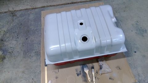 1983 Ford Bronco - A white fuel tank with red trim sits on a cardboard mat, ready for painting, with two brushes and a plastic bag of supplies.