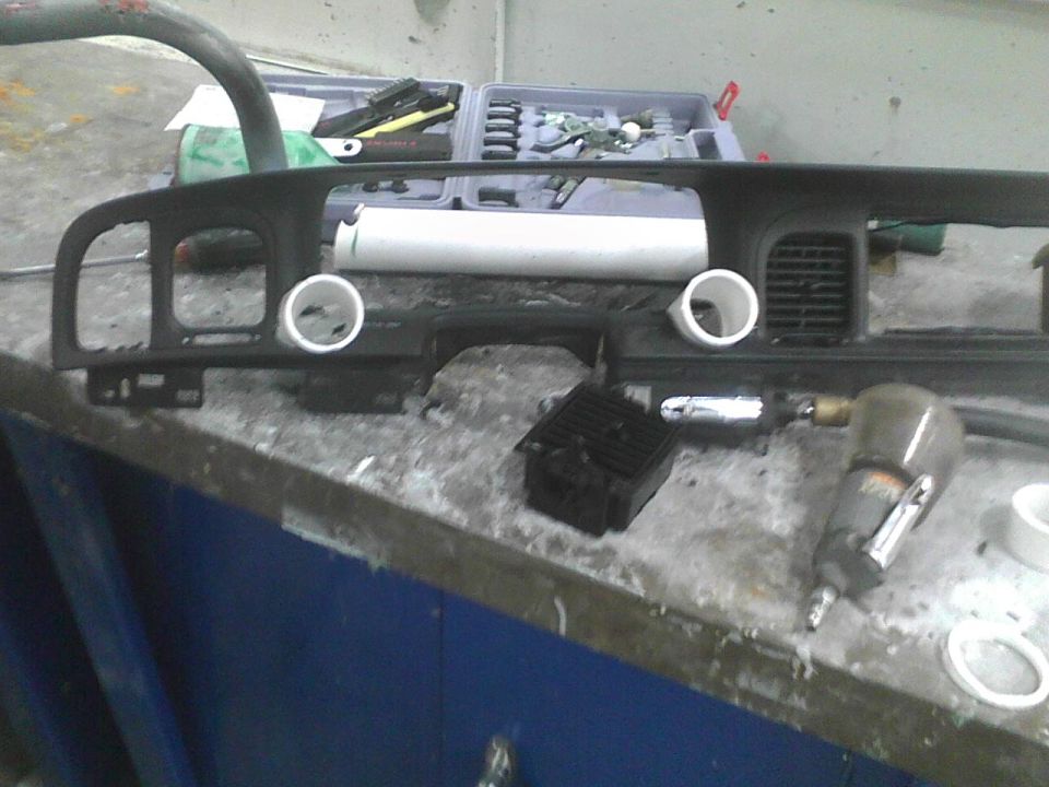 Car dashboard components on a workbench with tools, including an air-powered tool and a toolbox