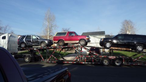 1995 Ford Bronco - A red Ford Bronco is transported on a car carrier alongside other vehicles under a clear blue sky.
