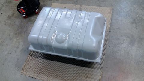 1983 Ford Bronco - A gray fuel tank sits on a piece of cardboard, with a black oil drain pan visible in the upper left corner.