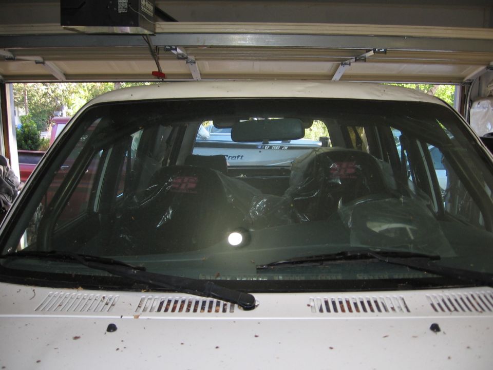 Interior view of a white SUV, seats covered in plastic. A boat is visible through the rear window
