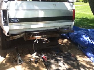 1996 Ford Bronco - The rear of a white Ford pickup truck is shown, with a trailer hitch and some tools on the ground.