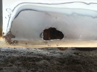 1996 Ford Bronco - Close-up of a damaged vehicle panel with visible rust and a hole, indicating wear and tear.