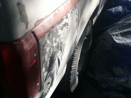 1996 Ford Bronco - Bodywork is underway on the rear of a vehicle, with primer and filler applied to the damaged area.